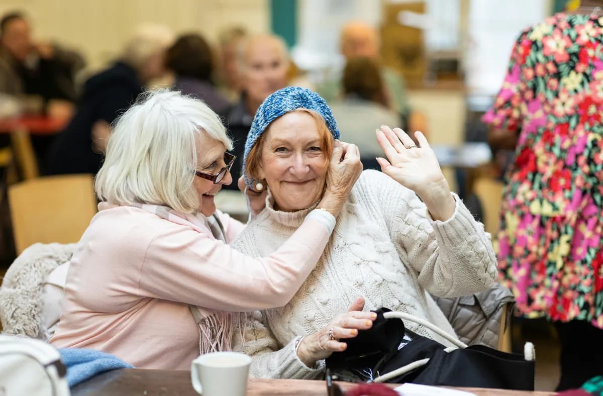 two elderly ladies hugging and smiling in a care home