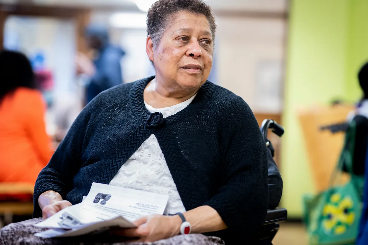 elderly lady sitting in a wheel chair reading a newspaper in a care home