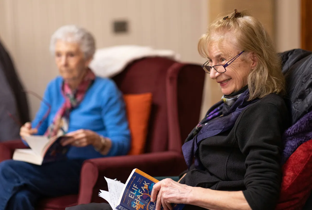 female staff of a care home reading and laughing with an elderly patient