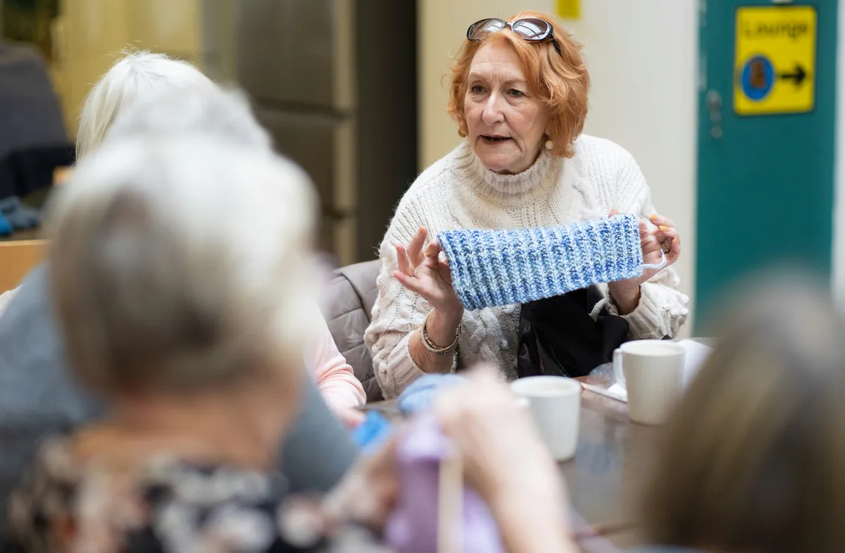 an elderly lady showing her knitted napkin to her friends in a care home